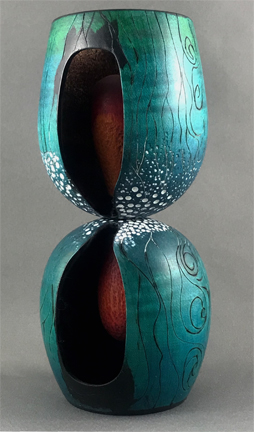 two wood-turned wine glass forms joined at their base to create a waited form. an hour-glass shape is carved out and inside we see the timer counting down. The outside is embellished with representations of polar ice, sea currents and wind